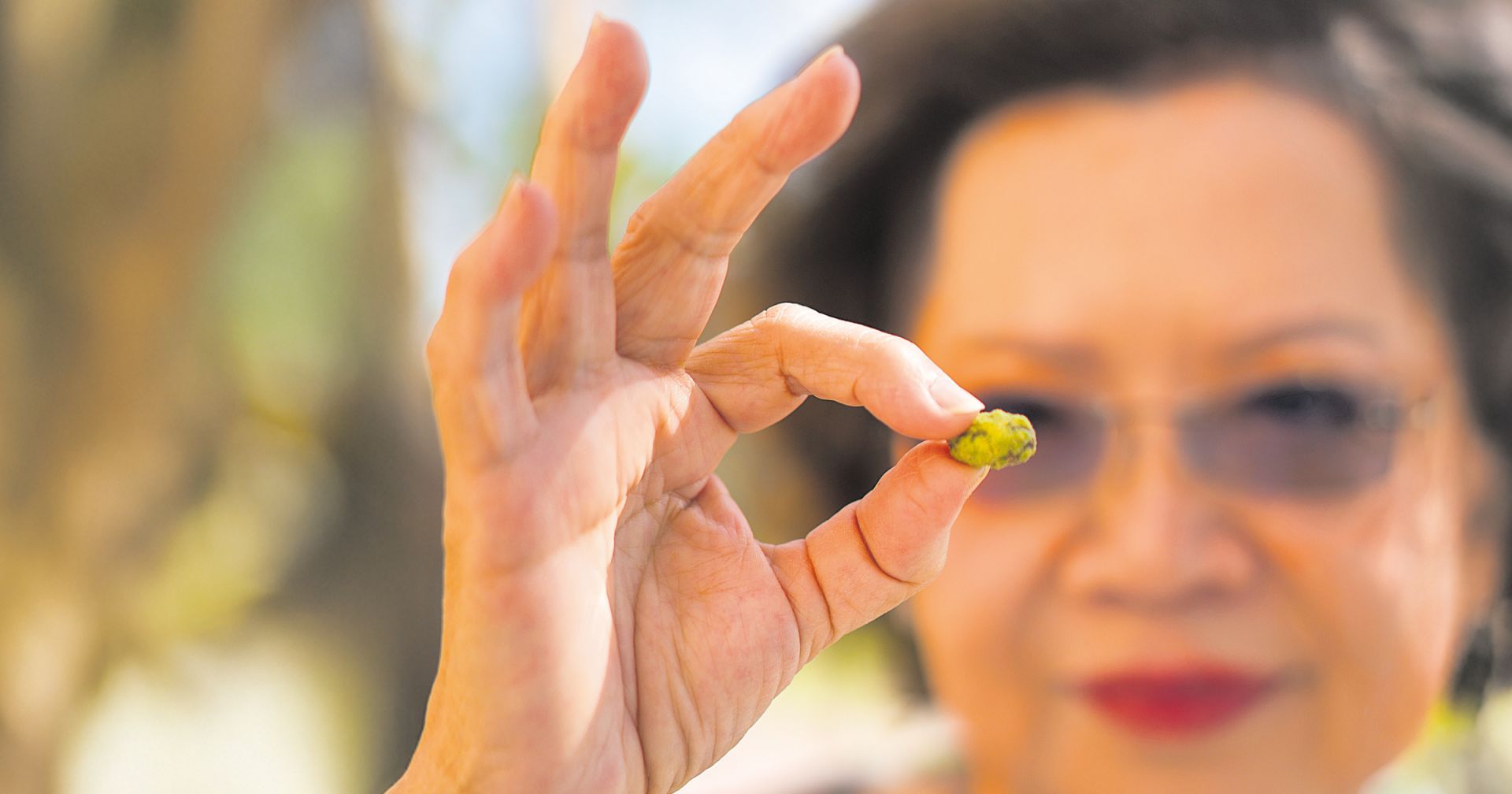 Eine Frau hält fokussiert eine kleine grüne Frucht zwischen ihren Fingern.