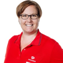 Porträtfoto einer lächelnden Frau mit Brille und rotem Poloshirt mit Firmenlogo vor weißem Hintergrund.