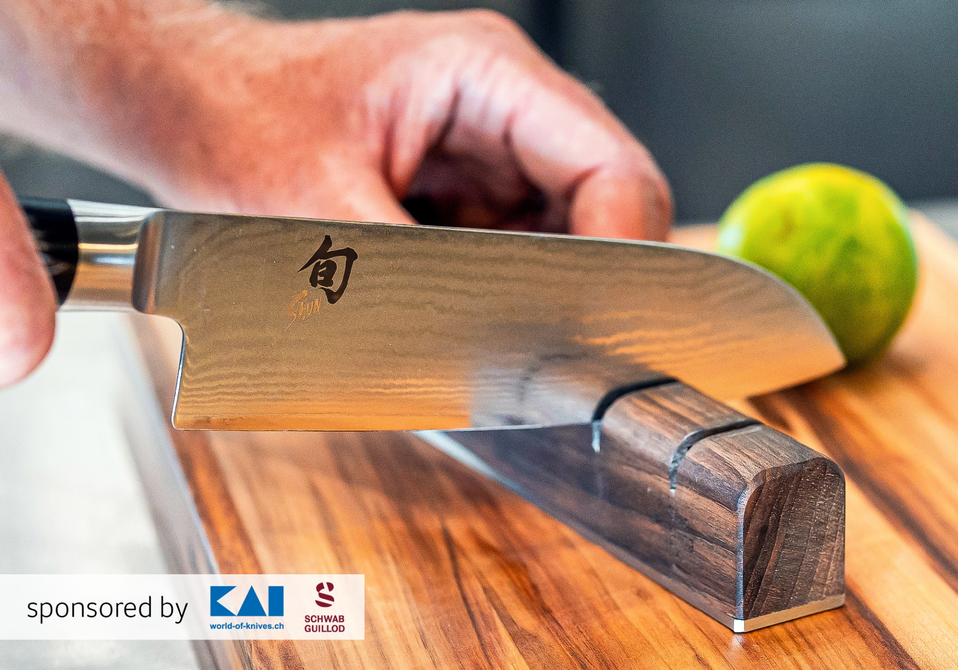 Nahaufnahme: Ein Messer wird auf einem Holzschleifblock geschärft; im Hintergrund eine unscharfe Limette.